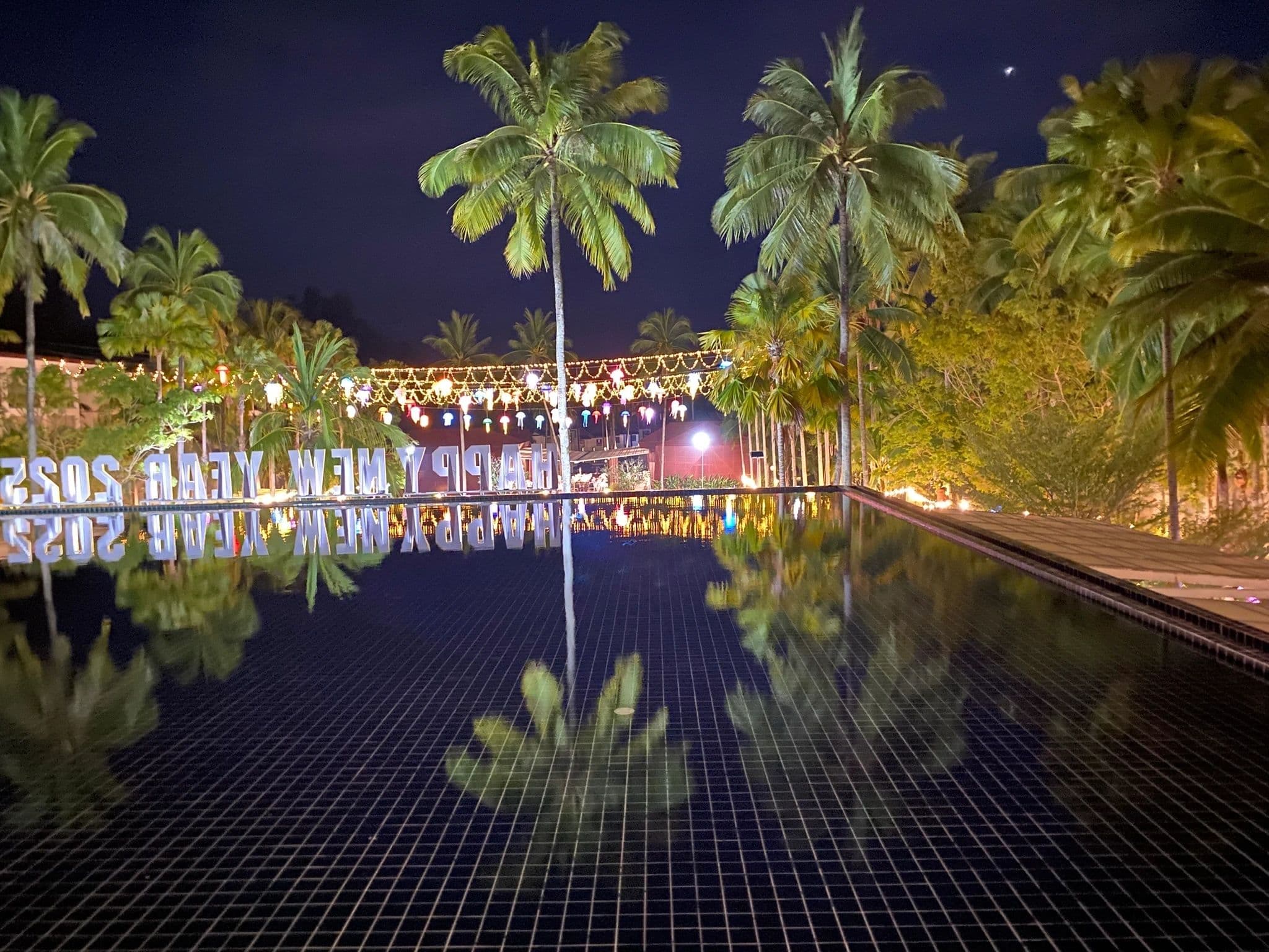 Happy New Year 2025 sign reflected in a resort pool at night